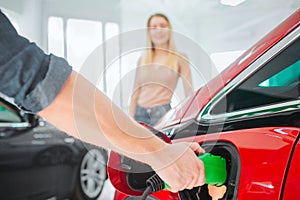 Young couple buying first electric car in the showroom. Close-up of hand charging electric car with the power cable