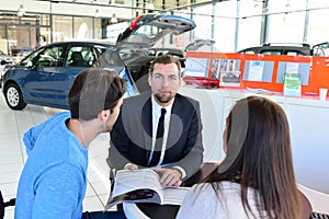 young couple buying a new car in the showroom of a car dealership - signature sales contract with seller