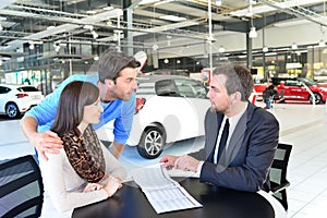 young couple buying a new car in the showroom of a car dealership - signature sales contract with seller