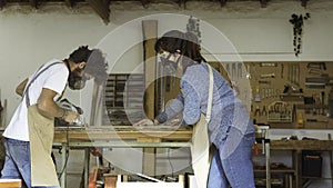 A young couple of carpenters working together in a small carpentry workshop designing a new home furniture piece crafting out of