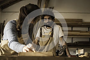 A young couple of carpenters working together in a small carpentry workshop designing a new home furniture piece crafting out of