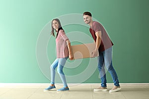 Young couple carrying big moving box at new home