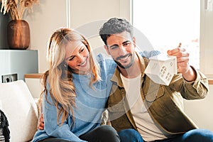 Young couple celebrating a beginning at their new home watching a little ornament house. Real estate investment