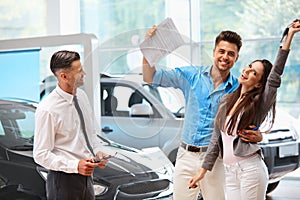 Young Couple Celebrating Purchase of a car In Car Showroom