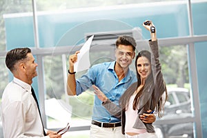 Young Couple Celebrating Purchase of a car In Car Showroom.