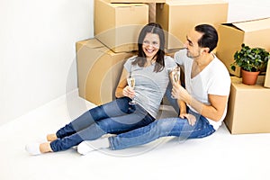 Young couple celebrating, sitting among boxes, drinking champange and plannig how they will furnish their new house.