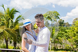 Young Couple With Cell Smart Phone Over Tropical Forest View Cheerful Man And Woman Using Smartphone Embracing
