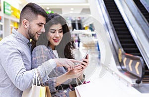 Young couple with cellphone making online order in mall