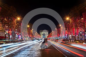 Young couple on Champs Elysees avenue and the Arc de Triomphe decorated with red Christmas lights at night  in Paris France. Chri