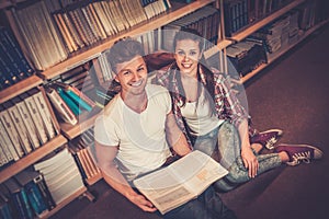 Young couple of cheerful students sitting on the floor and studying in the university library.