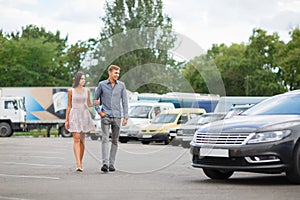 A young couple chooses their first car. Lovers walk around the caravan and look at cars.q