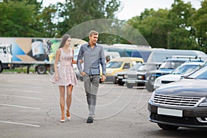 A young couple chooses their first car. Lovers walk around the caravan and look at cars.q