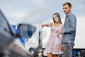 A young couple chooses their first car. Lovers walk around the caravan and look at cars.q