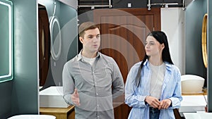 Young couple choosing new bathroom furniture at the plumbing shop with lots of sanitary goods