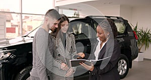 Young couple choosing new car for buying in dealership shop