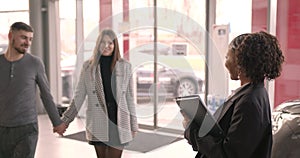 Young couple choosing new car for buying in dealership shop