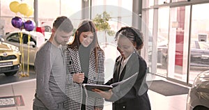 Young couple choosing new car for buying in dealership shop