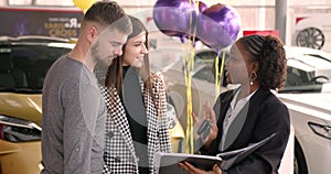 Young couple choosing new car for buying in dealership shop