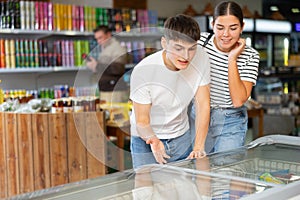 Young couple choosing products in refrigerated display case in food store