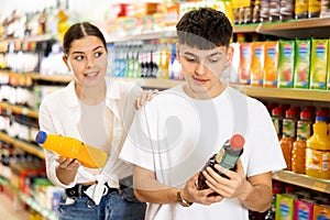 Young couple choosing sweet fruit juices in supermarket