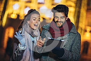 Couple in the city centre with holiday`s brights in background. Couple browsing digital tablet. They are using credit card