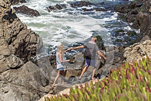 Young couple climbing the rocks and enjoying the view along the rugged Big Sur coastline.