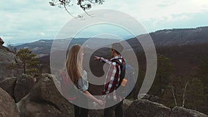 Young couple climbing the rocky hills, stylish young man with a backpack gives a hand to his beautiful girlfriend with a