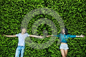 Young couple is closing his eyes back on the bright green foliage. Arms spread wide, hands reaching out to each other. Top view.
