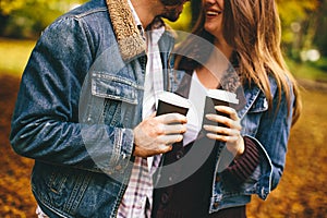 Young couple with coffee cups walking in autumn park