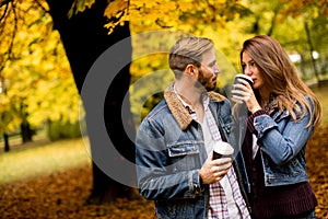 Young couple with coffee cups walking in autumn park