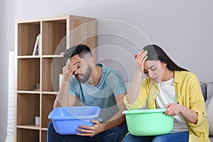 Young couple collecting leaking water from ceiling at home. Time to call roof repair service