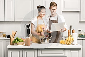 young couple cooking pasta and using laptop