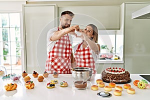 Young couple cooking pastries at the kitchen smiling in love showing heart symbol and shape with hands