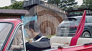 Young couple in countryside area sitting together in a car. Stock. Red flag on a back seat, retro car in a village.