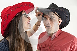 Young couple with cowboy hats and glasses making silly faces on white