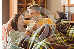 Young couple cuddling on the couch under blanket