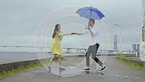 Young couple dance swiftly under umbrella on a pier on a sea coast
