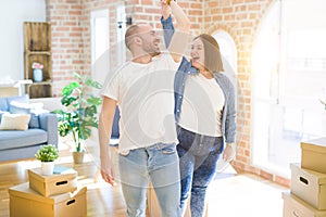 Young couple dancing around cardboard boxes at new home, celebrating smiling very happy new house