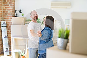 Young couple dancing around cardboard boxes at new home, celebrating smiling very happy new house