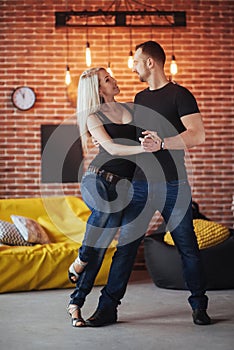 Young couple dancing latin music: Bachata, merengue, salsa. Two elegance pose on cafe with brick walls