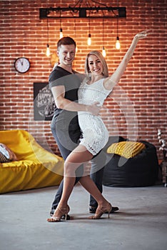 Young couple dancing latin music: Bachata, merengue, salsa. Two elegance pose on cafe with brick walls