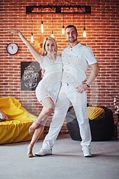 Young couple dancing latin music: Bachata, merengue, salsa. Two elegance pose on cafe with brick walls