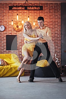 Young couple dancing latin music: Bachata, merengue, salsa. Two elegance pose on cafe with brick walls