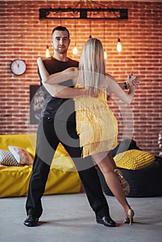 Young couple dancing latin music: Bachata, merengue, salsa. Two elegance pose on cafe with brick walls