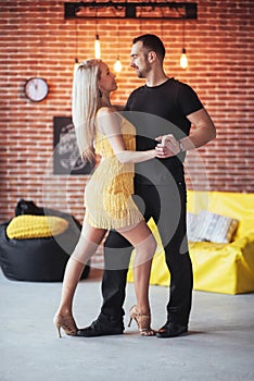 Young couple dancing latin music: Bachata, merengue, salsa. Two elegance pose on cafe with brick walls