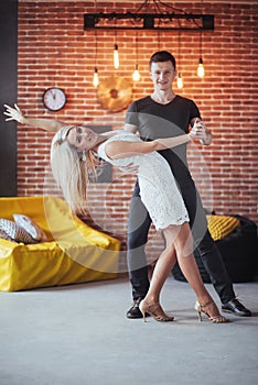 Young couple dancing latin music: Bachata, merengue, salsa. Two elegance pose on cafe with brick walls