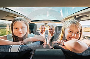 Young couple with daughters portrait sitting in a modern car with a transparent roof. Happy family moments, childhood, fast food