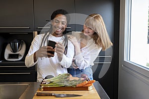 Young couple of different ethnic groups with mobile phone in a kitchen with vegetable board. concept of healthy living