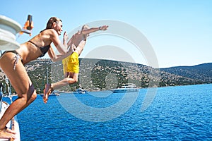 Young couple diving into the turquoise water of the sea from yacht.