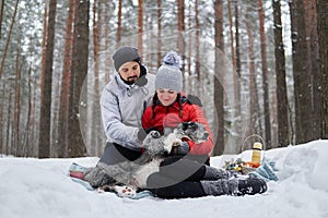 Young couple with dog have picnic in snowy forest